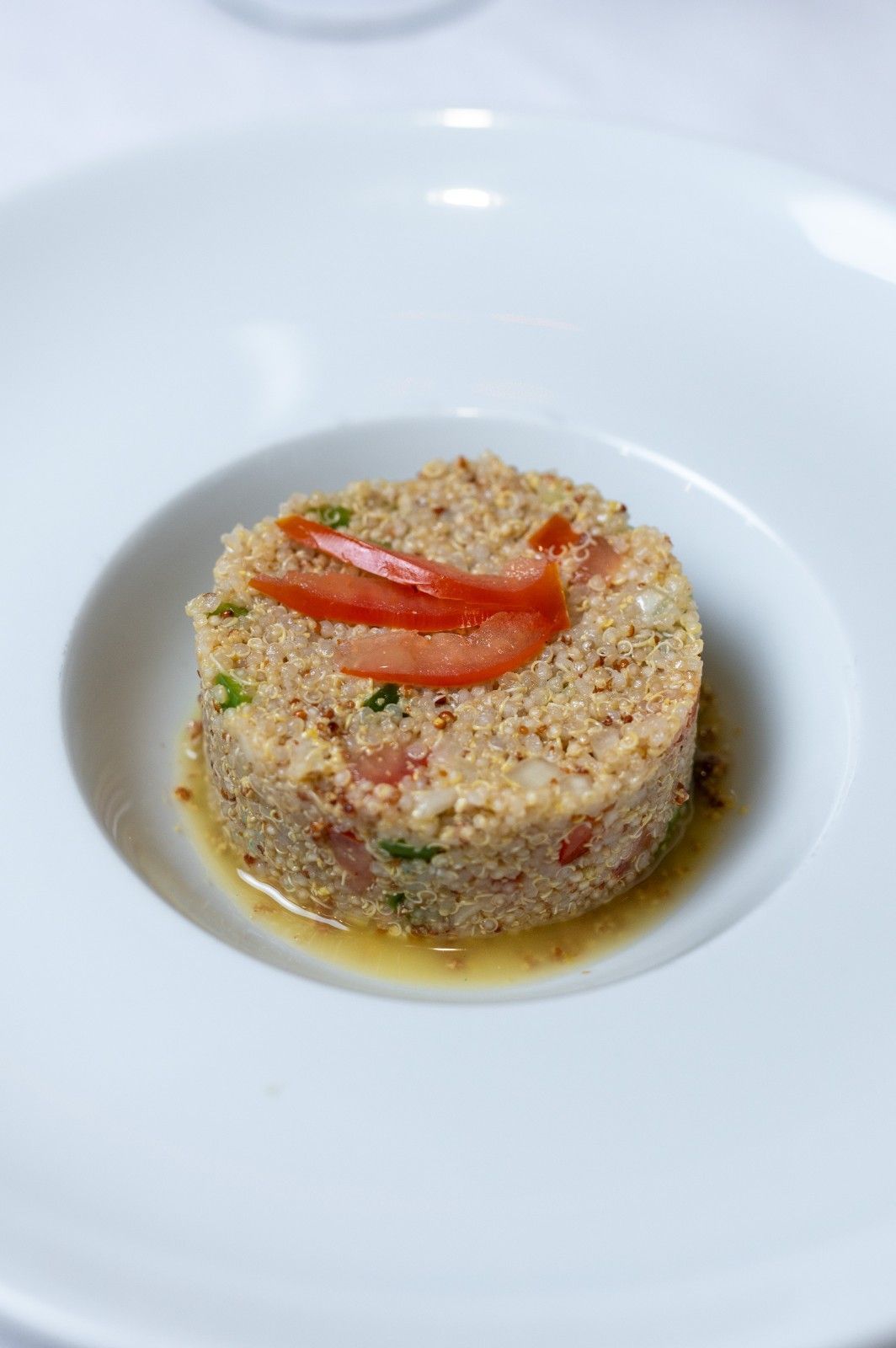Timbal de quinoa adornado con tiras de pimiento rojo, servido en un tazón blanco con una salsa ligera.