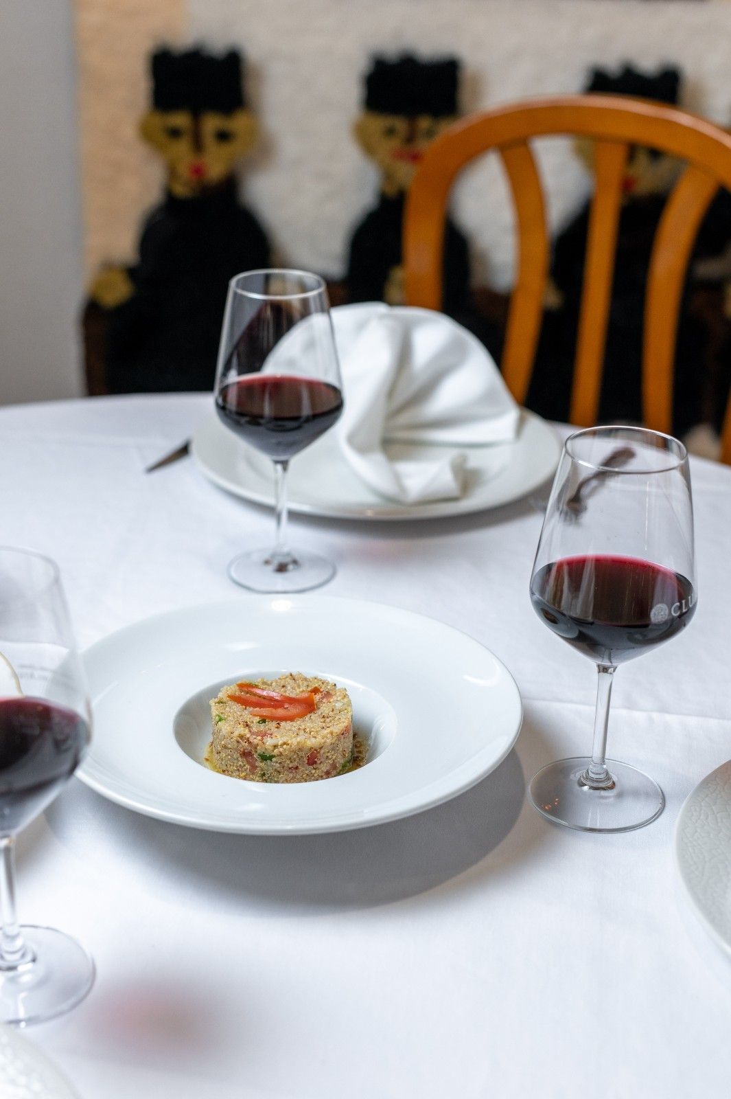 Elegante mesa de comedor con copas de vino y un aperitivo emplatado, dispuesta con servilletas blancas dobladas.