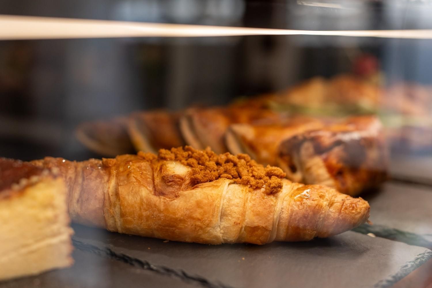 Pasteles recién hechos en una vitrina de panadería, con un cruasán dorado en primer plano.