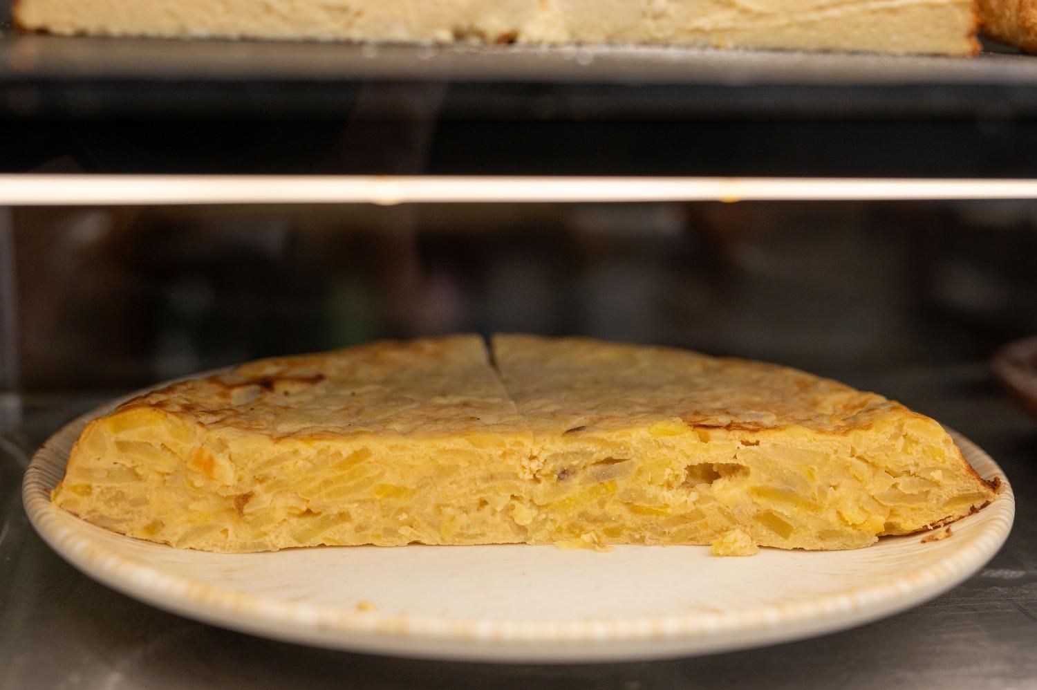 Tortilla redonda dorada sobre un plato blanco dentro de una vitrina.