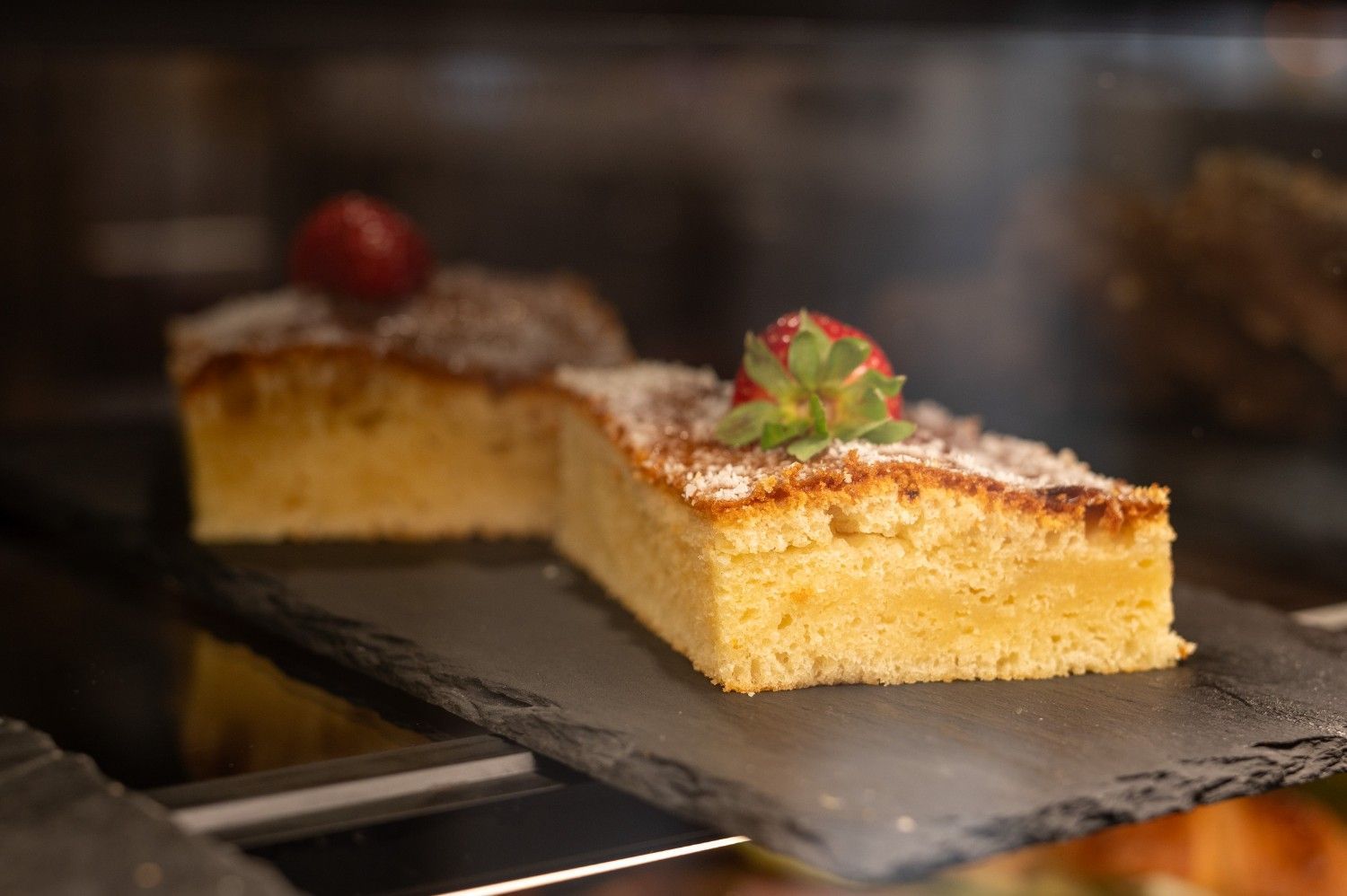 Dos rebanadas de pastel en una bandeja de pizarra, cubiertas con azúcar glas y fresas.
