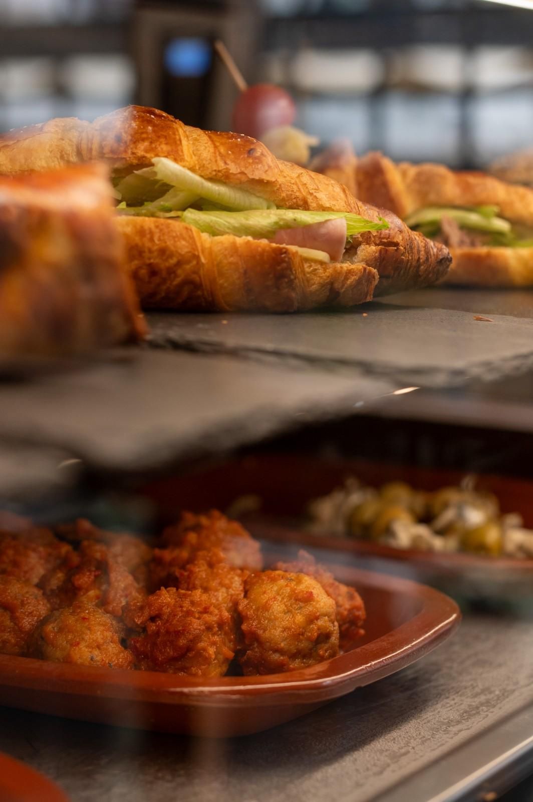 Bandeja de pasteles y bocadillos fritos expuestos en el mostrador de una panadería, con un cruasán como protagonista.