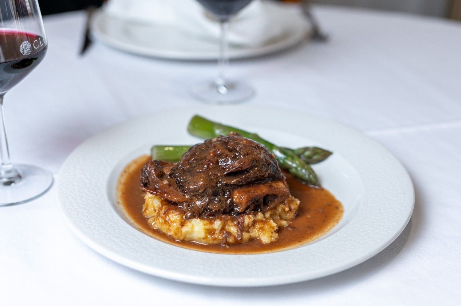 Carne estofada con judías verdes sobre puré de patatas en salsa marrón, servida sobre un mantel blanco.