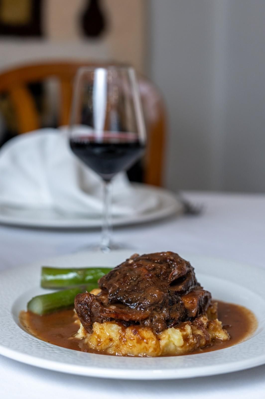 Plato de carne de res con verduras y vino tinto servido en una mesa de un restaurante.