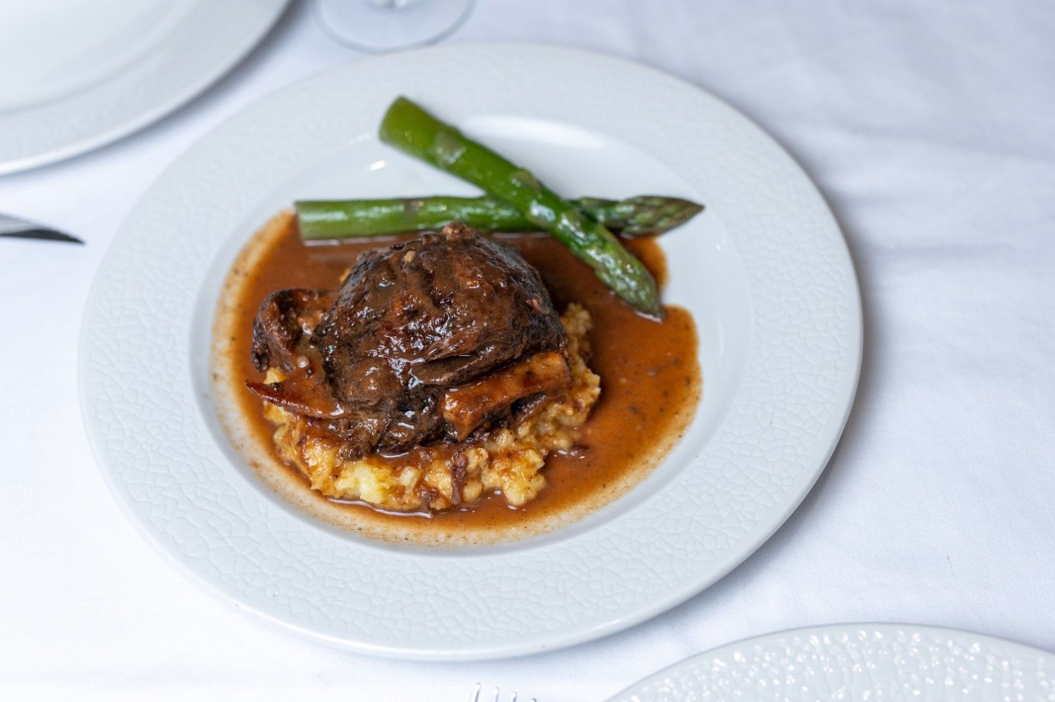 Carne estofada con salsa, judías verdes y guarnición crujiente en un plato blanco.