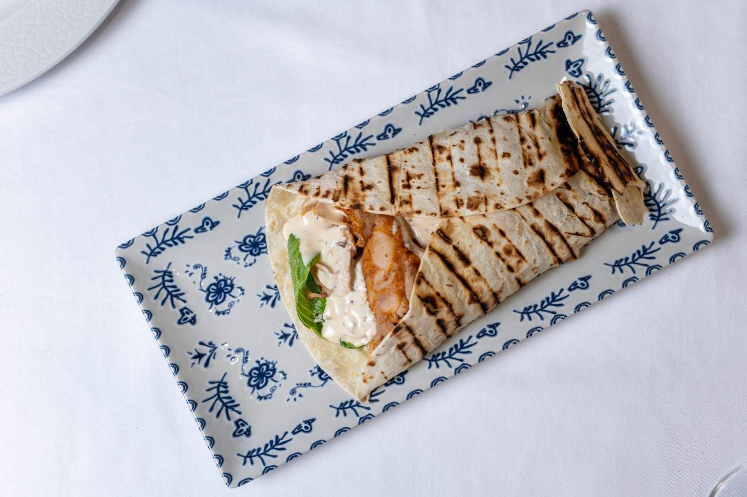 Sándwich de wrap a la parrilla en un plato con estampado azul y blanco sobre un mantel blanco.