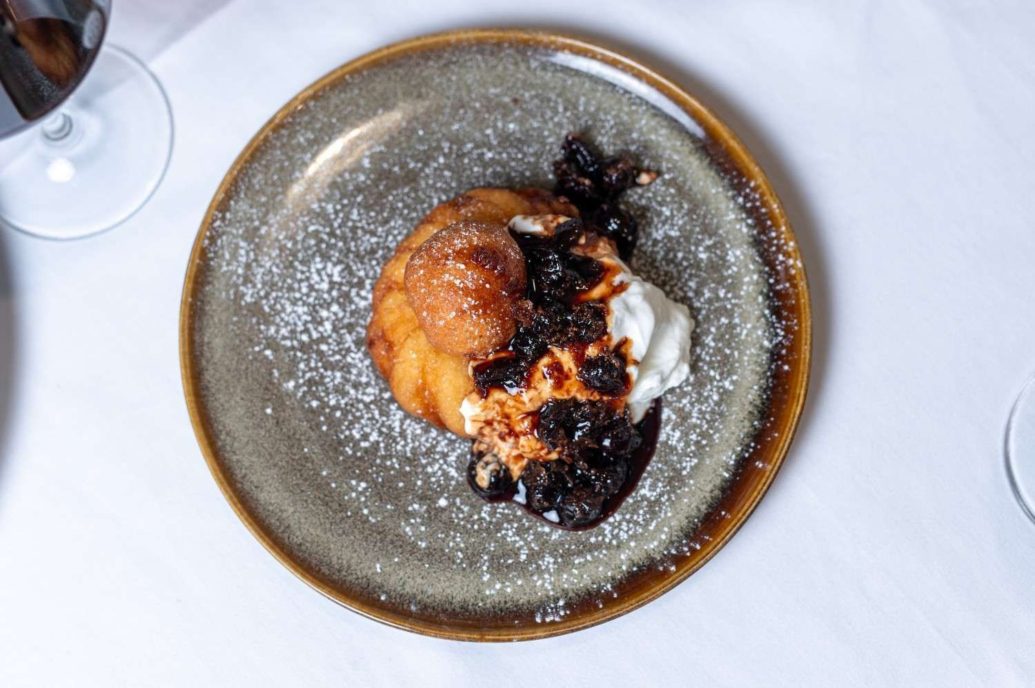 Postre en un plato gris con azúcar glas y salsa de frutos rojos oscuros, sobre un mantel blanco.