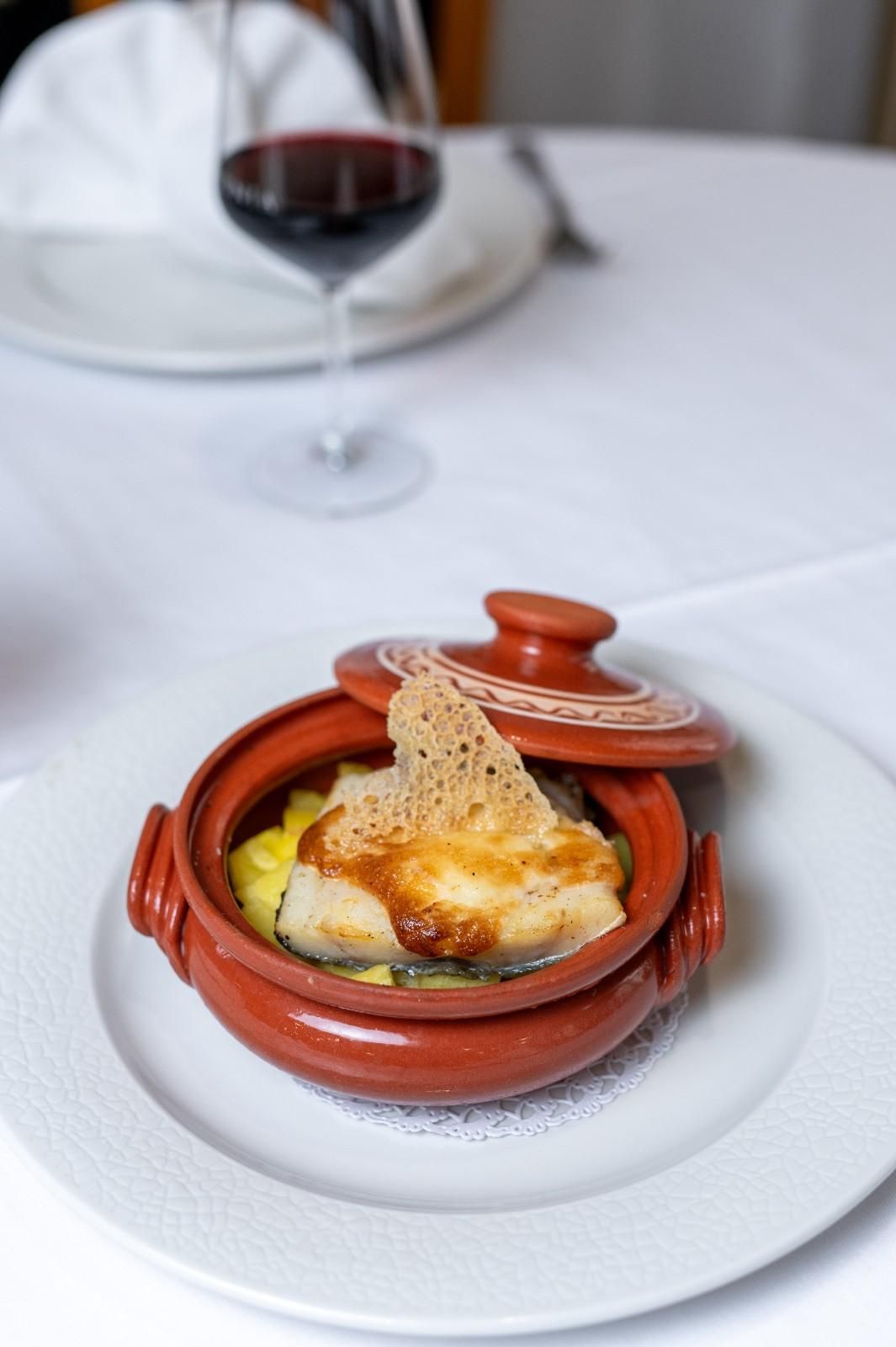 Una pequeña olla de barro con comida horneada sobre un plato blanco en la mesa de un restaurante.