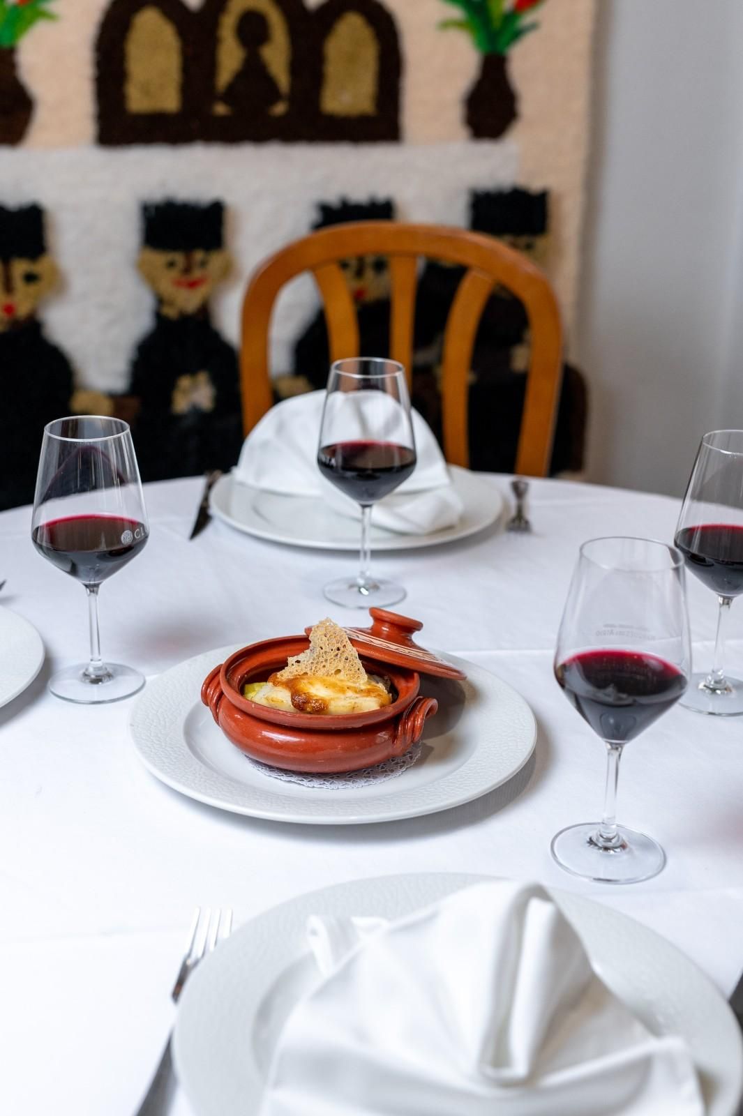 Elegante mesa de comedor puesta con copas de vino, servilletas blancas y una paellera en un acogedor restaurante.