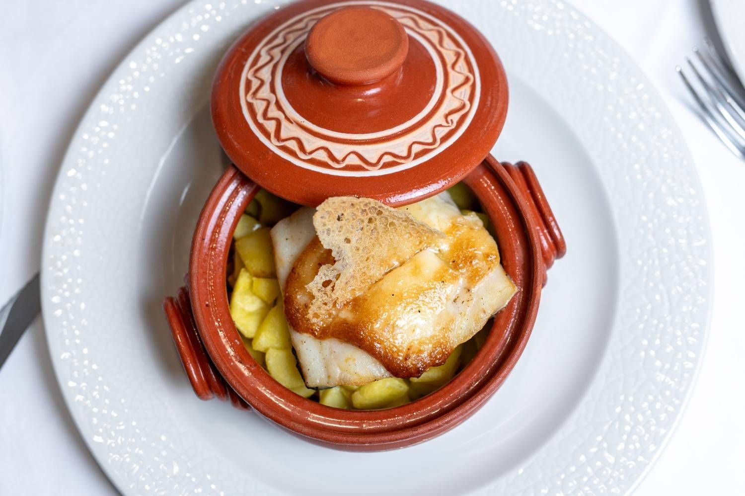 Plato de cazuela de barro con pescado, patatas y zanahorias sobre un plato blanco.