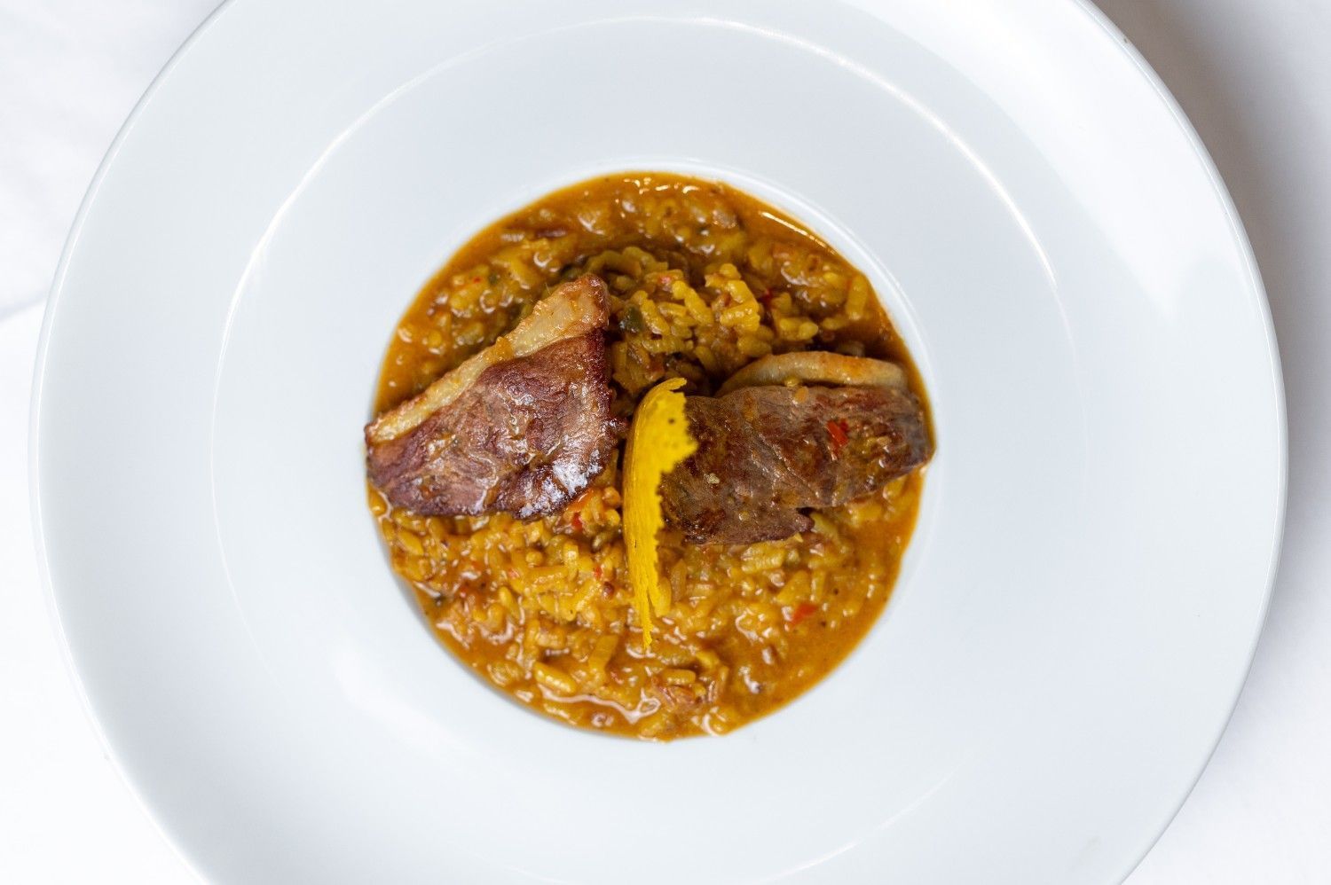 Bol blanco con un plato de arroz en salsa, cubierto con dos trozos de carne y una guarnición amarilla.