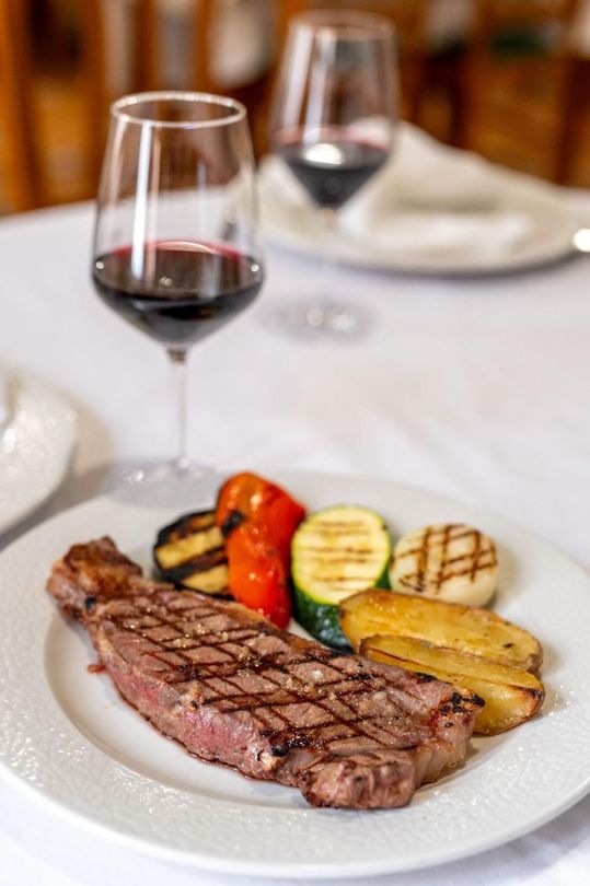 Filete a la parrilla con verduras y vino tinto sobre un mantel blanco en un restaurante.