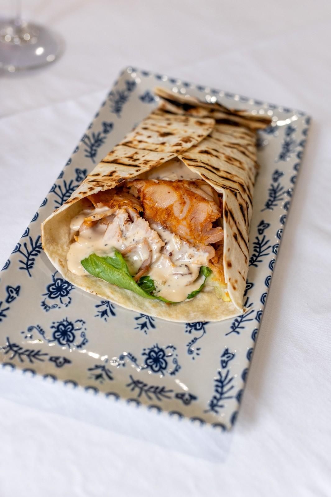 Wrap a la parrilla con pollo y lechuga a la vista en un plato azul y blanco.