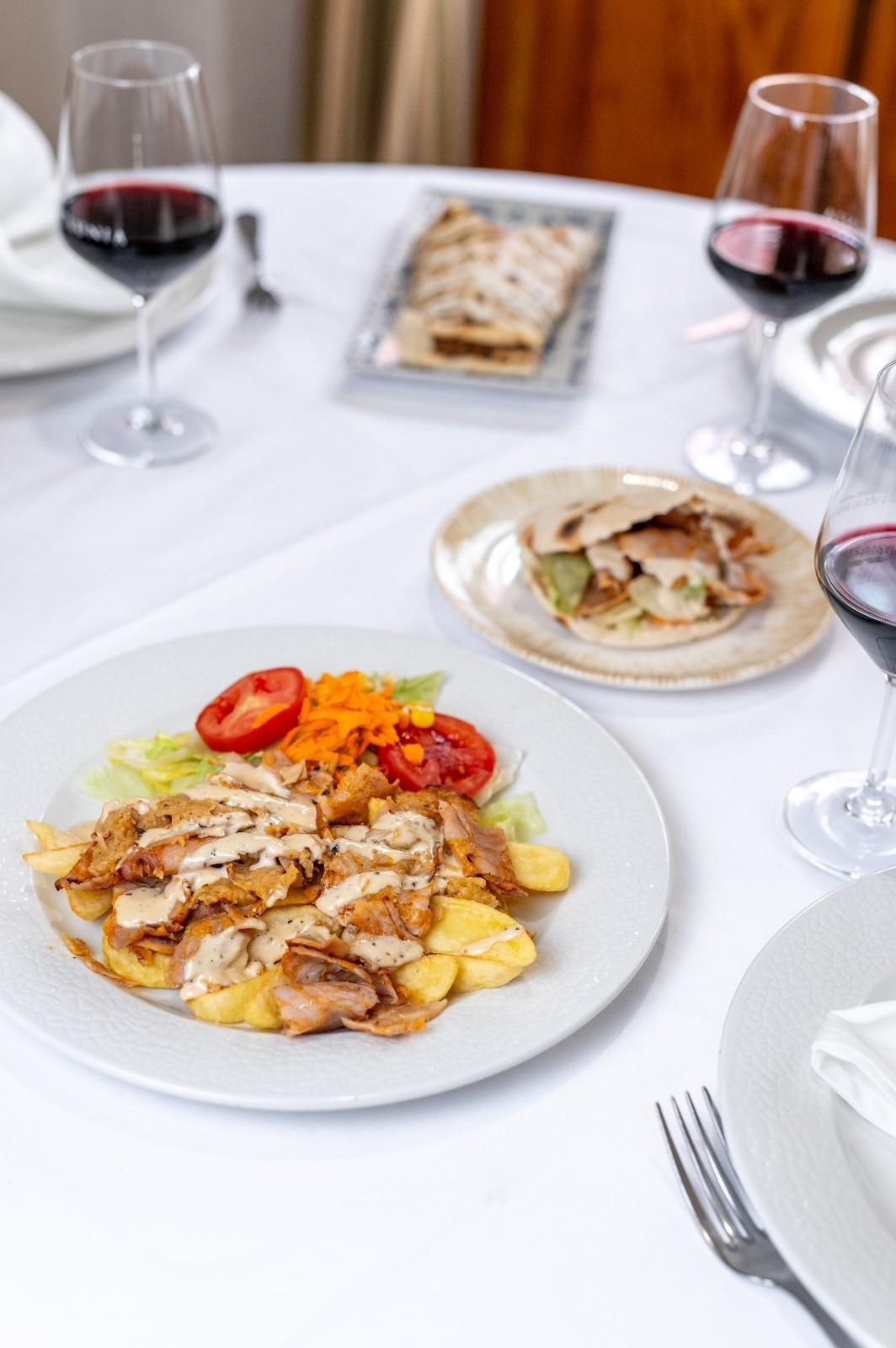 Elegante mesa puesta con platos de pescado y verduras, copas de vino y un mantel blanco.