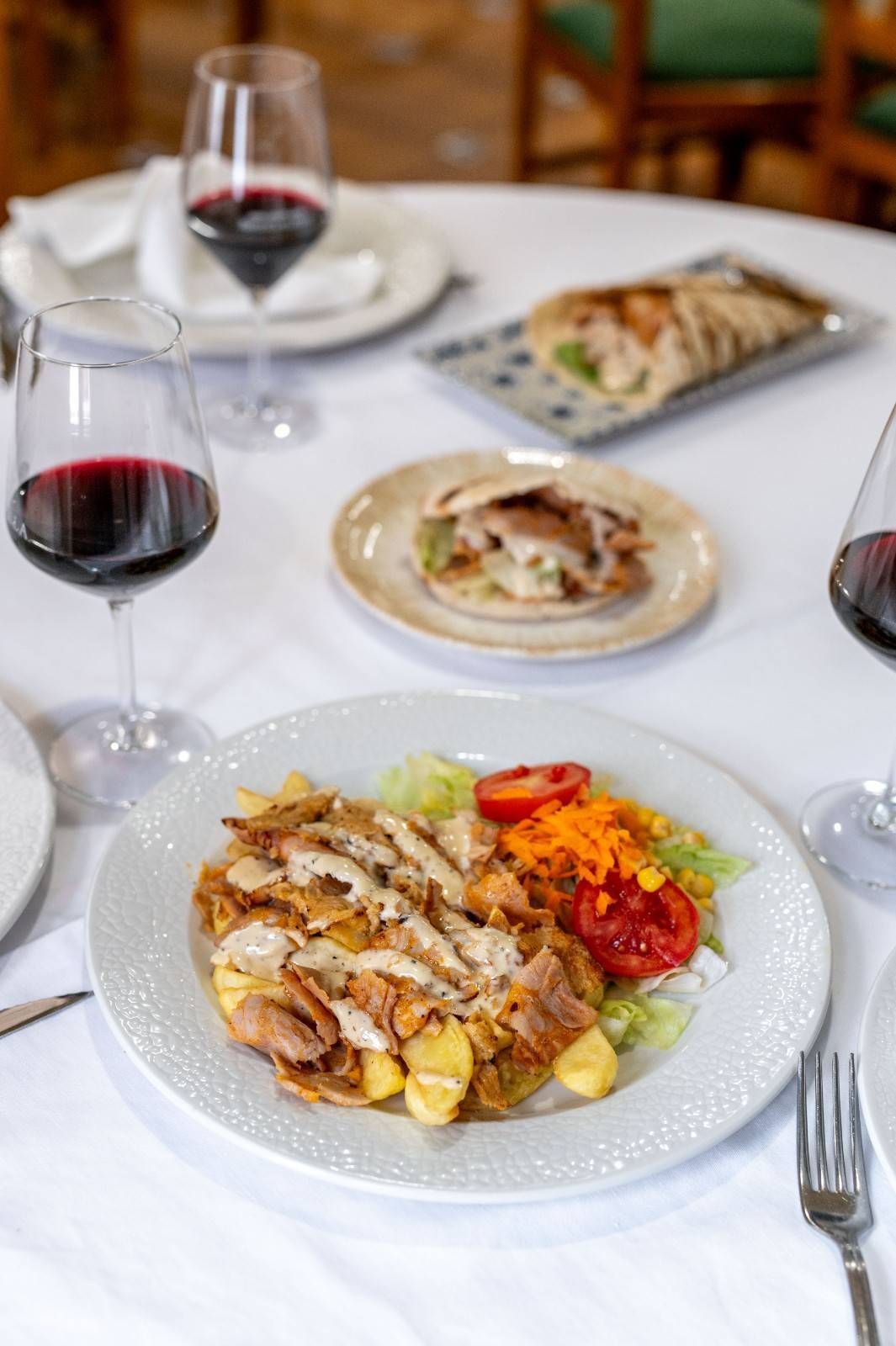 Platos de pasta emplatados y copas de vino tinto sobre una mesa de restaurante cubierta con un mantel blanco.