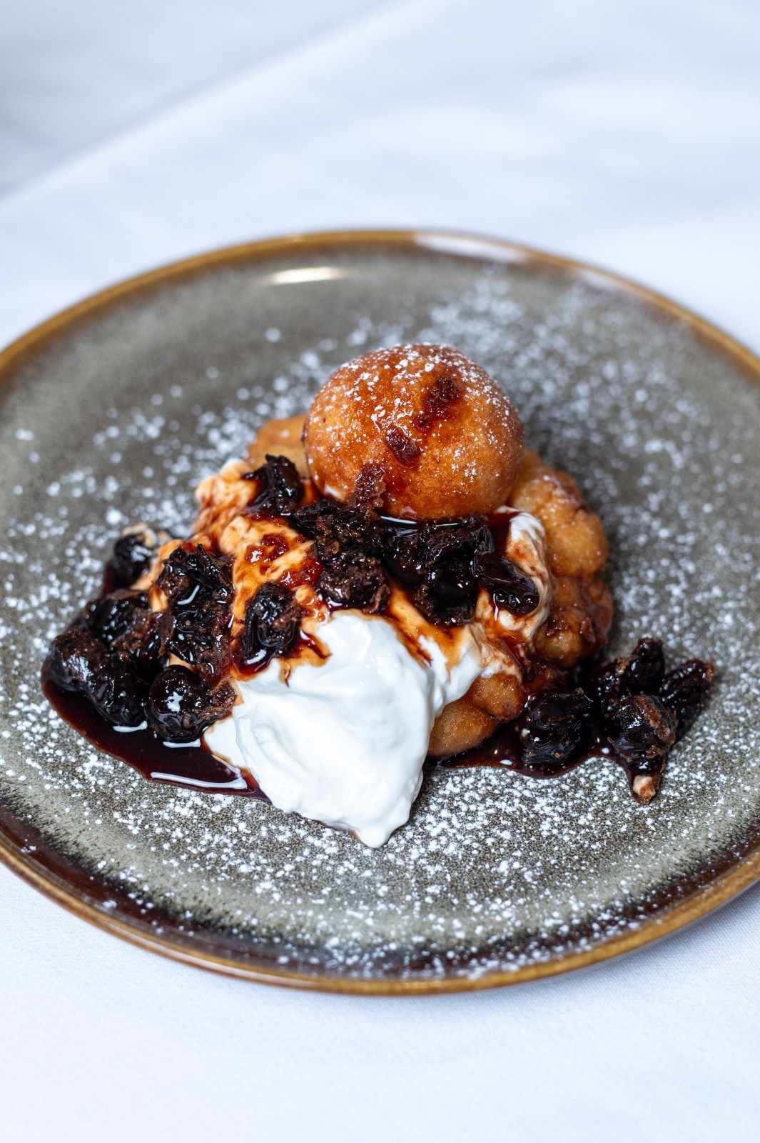 Postre en un plato moteado con crema batida y salsa oscura sobre un mantel blanco.