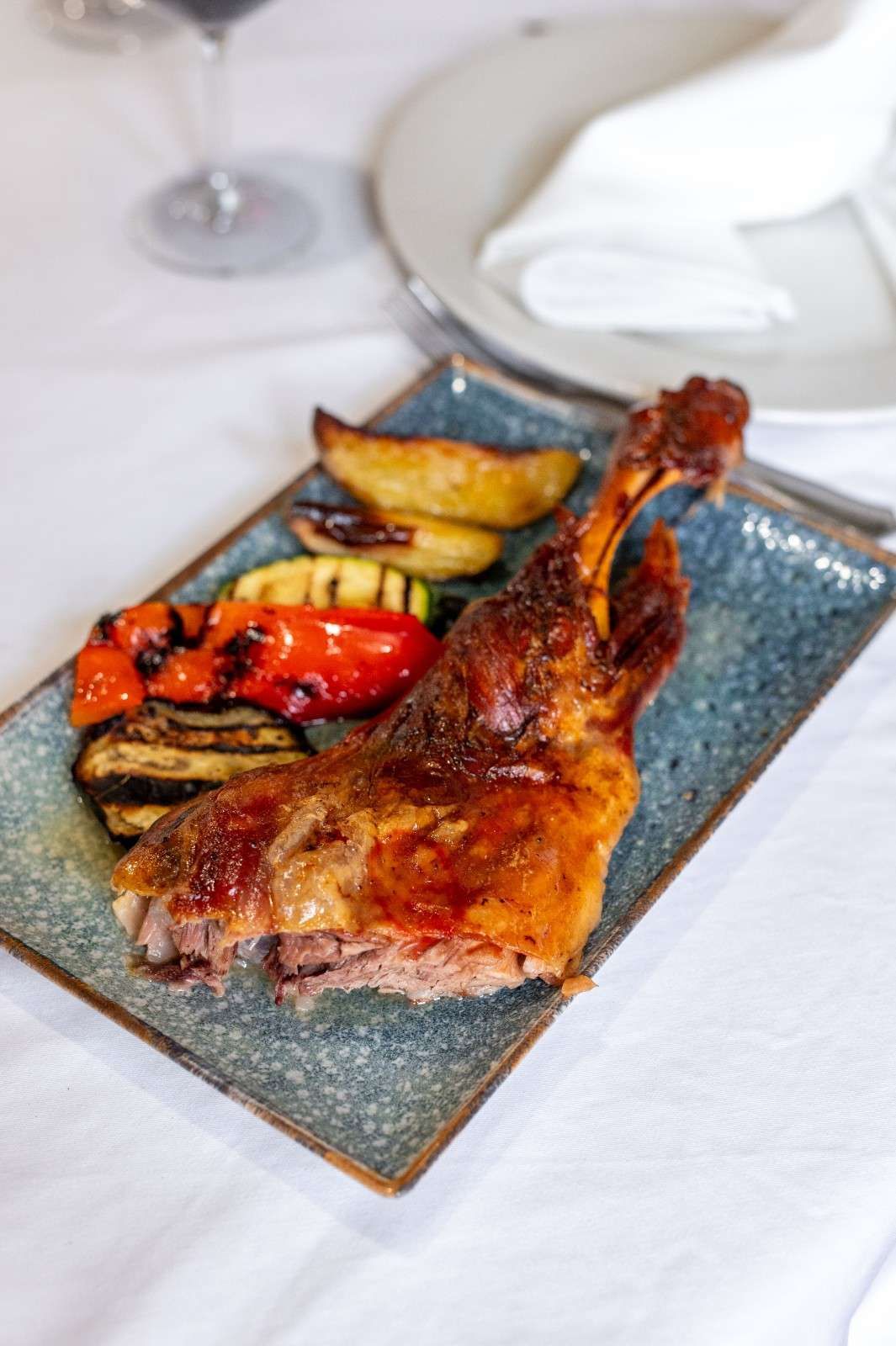Carne a la parrilla con verduras asadas en un plato rectangular sobre una mesa.