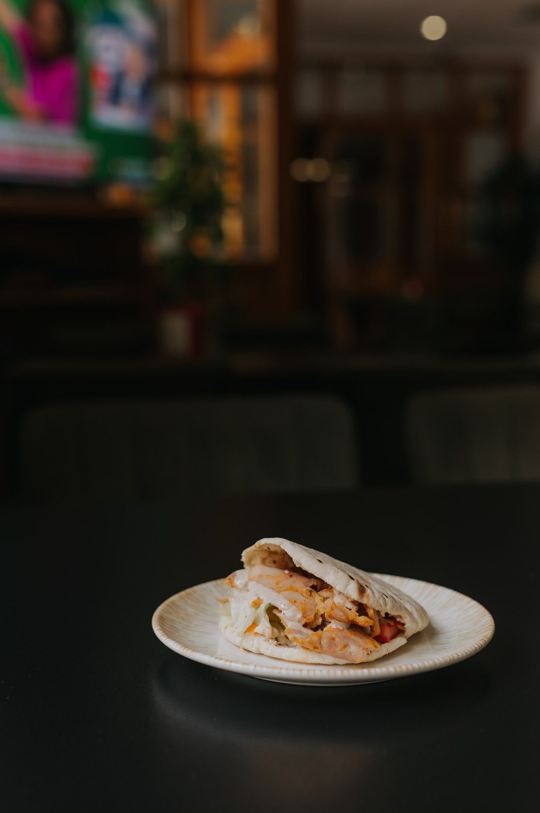 Un sándwich en un plato blanco sobre una mesa oscura en un restaurante con poca luz.