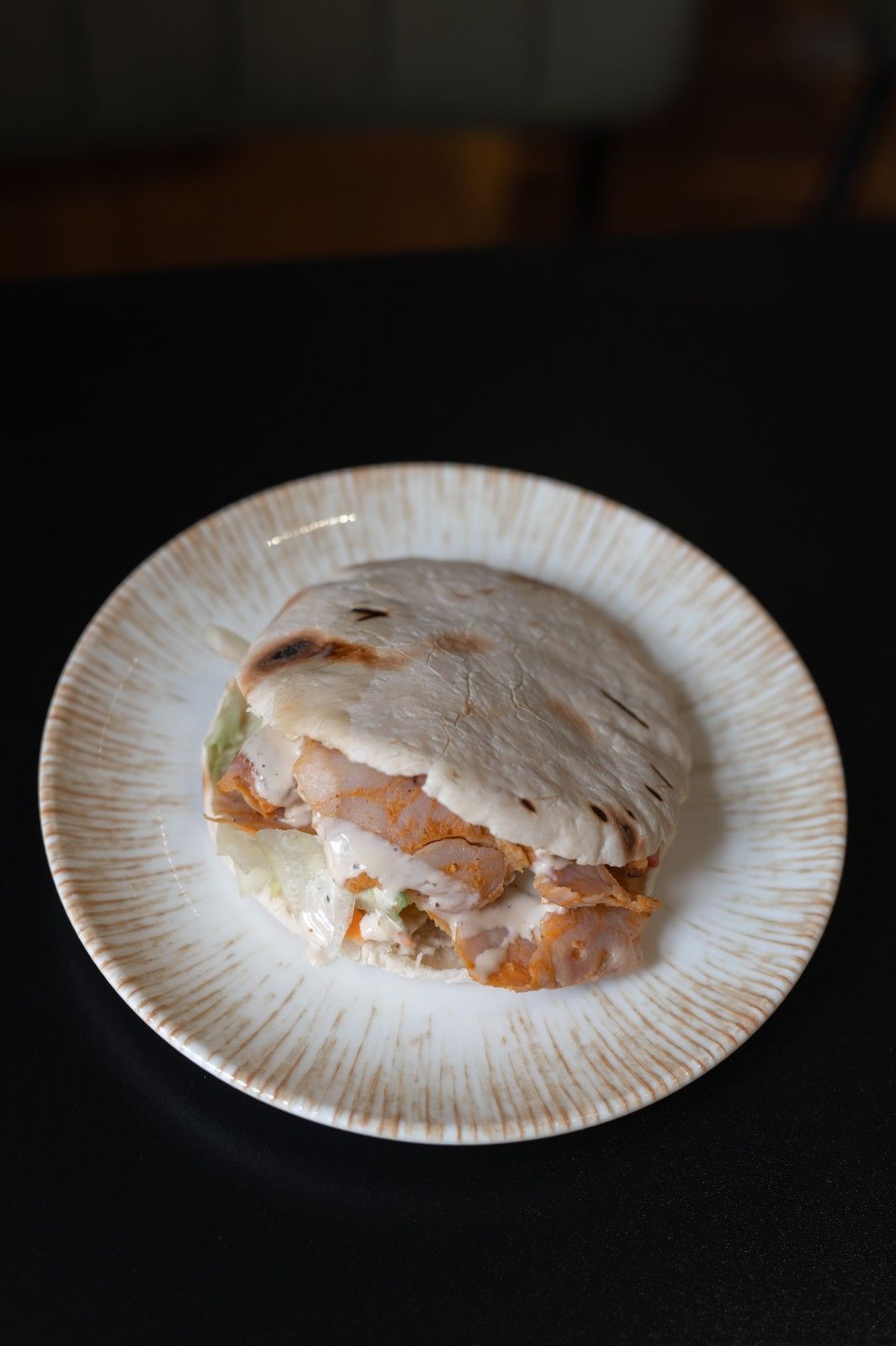 Sándwich parcialmente comido en un plato blanco sobre una mesa oscura.