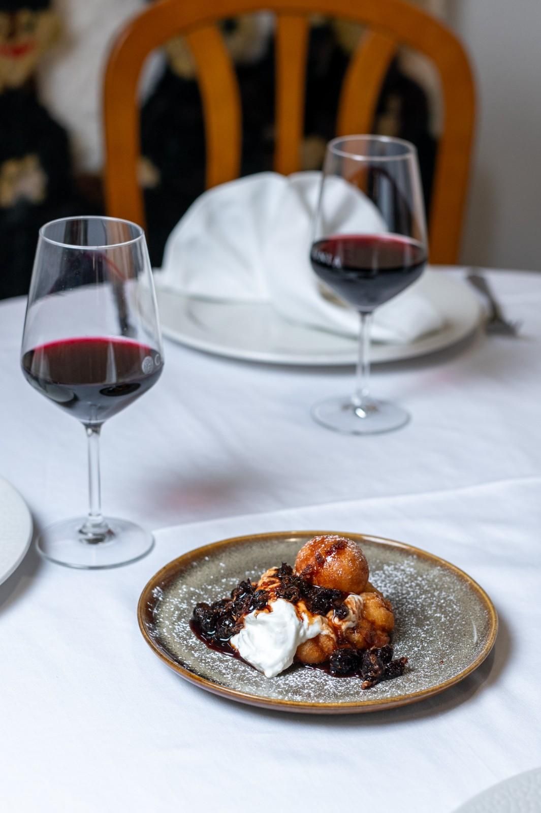 Postre en un plato moteado con crema batida y frutos rojos en una mesa de restaurante con dos copas de vino tinto.