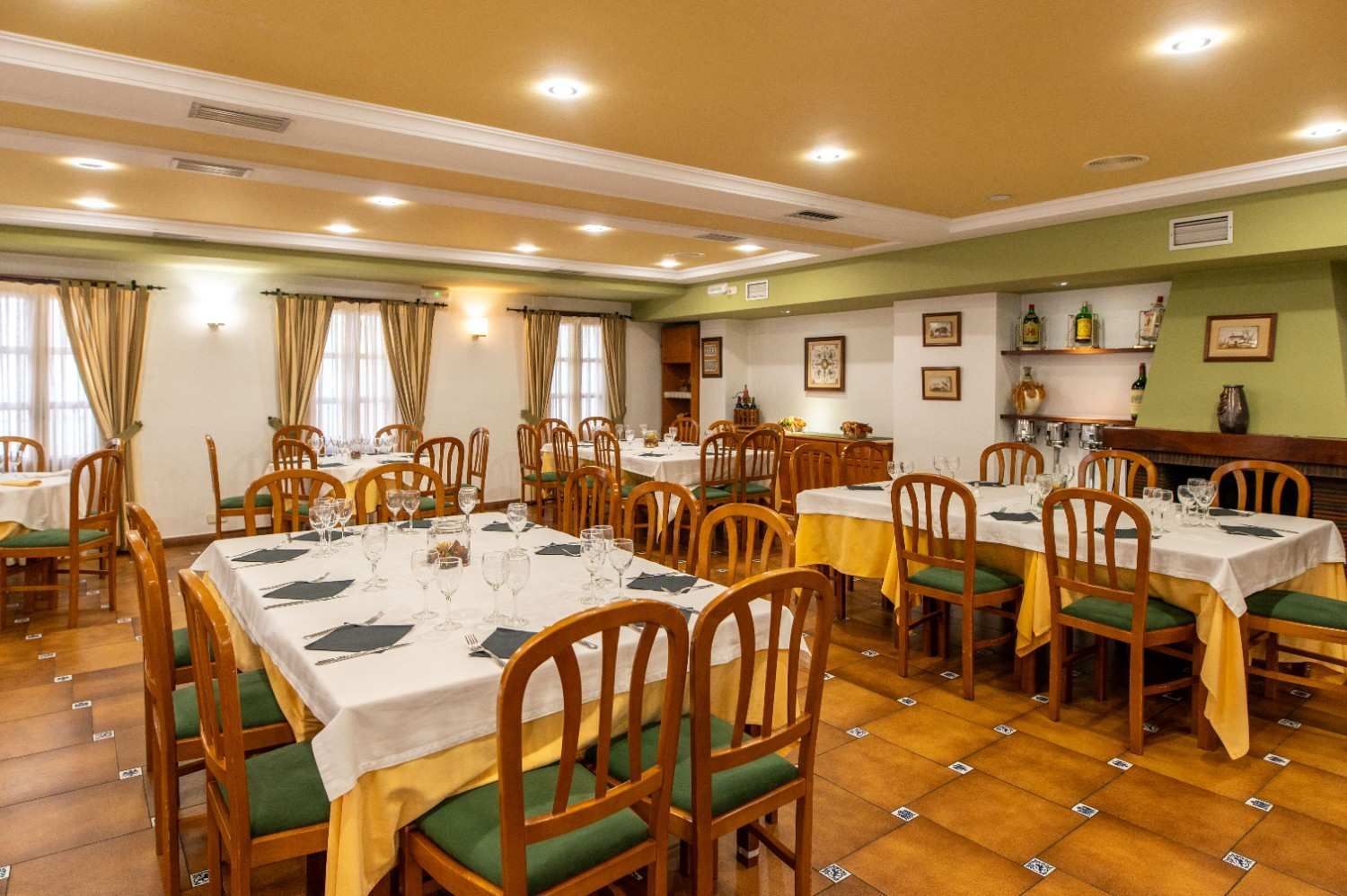 Comedor vacío con sillas de madera, manteles blancos y una cálida iluminación amarilla.