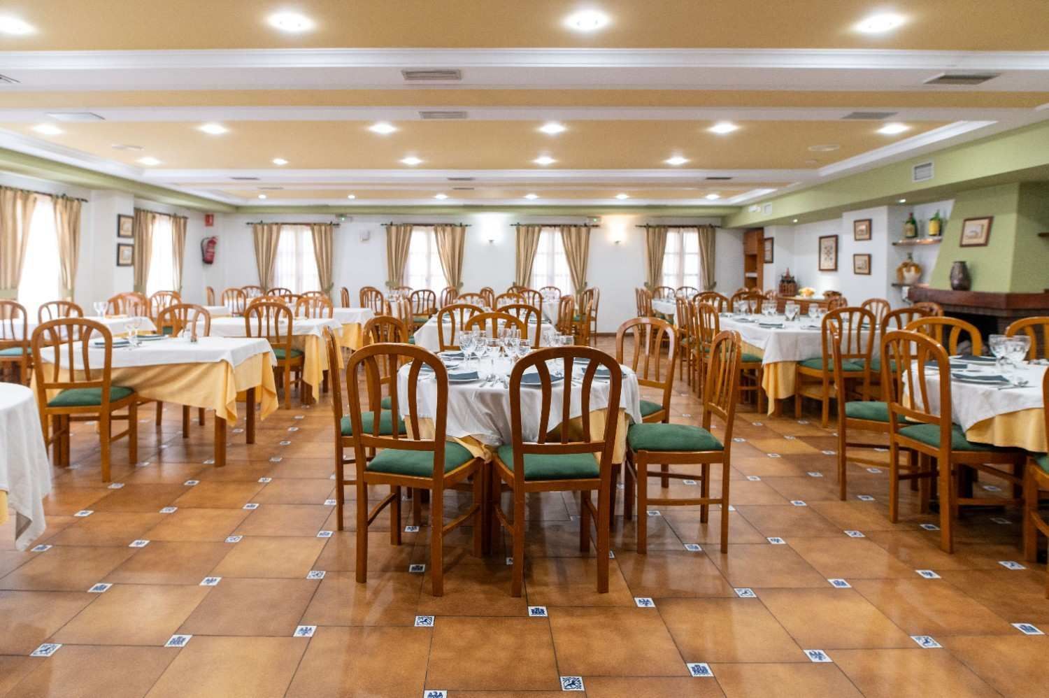 Comedor vacío de un restaurante con sillas de madera, manteles blancos y una iluminación cálida en el techo.