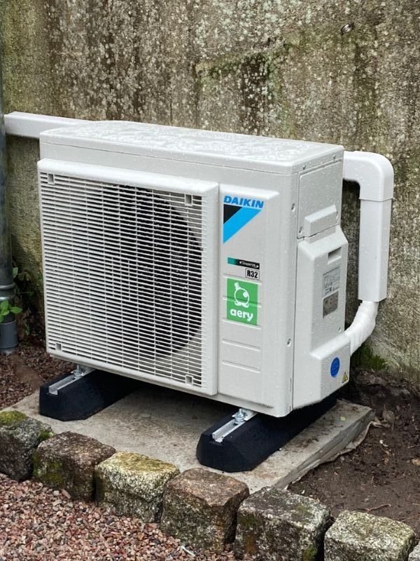Radiateur blanc fixé au mur d'une pièce, avec des tuyaux en cuivre et un thermostat.