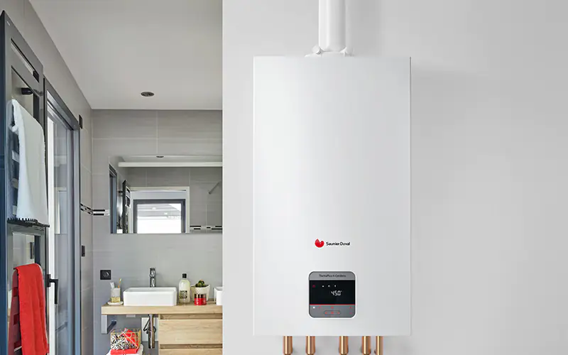 Chaudière à gaz murale blanche avec présentoir dans une salle de bains moderne ; tuyaux en cuivre en dessous.