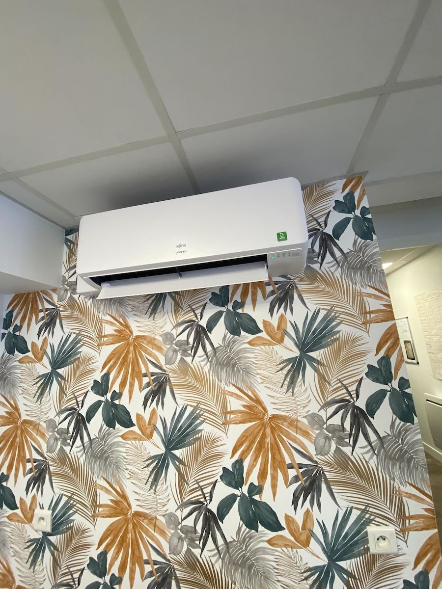 Climatiseur blanc fixé sur un papier peint à motifs botaniques.