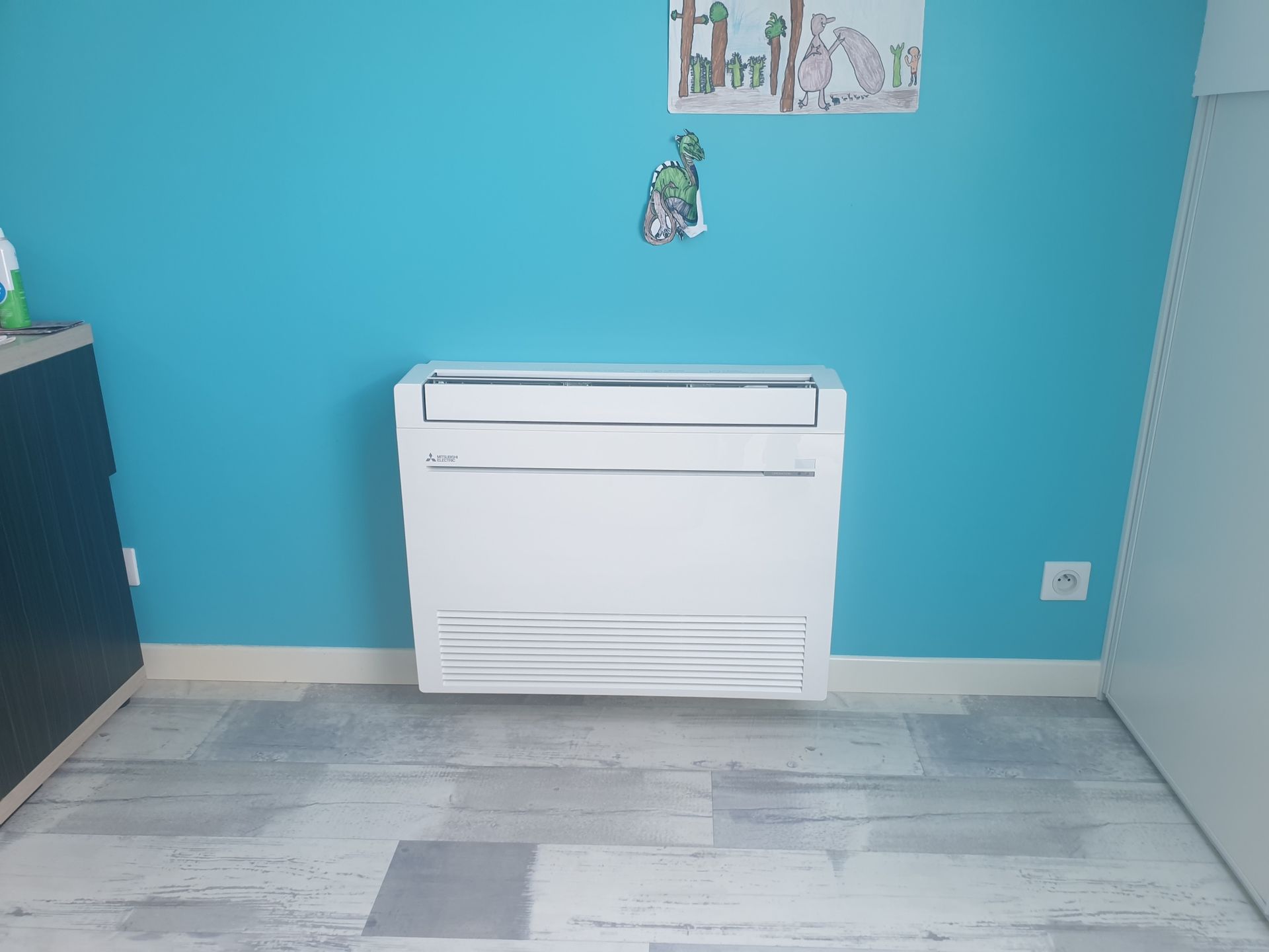 Unité de climatisation blanche sur un mur bleu dans une pièce au parquet clair.