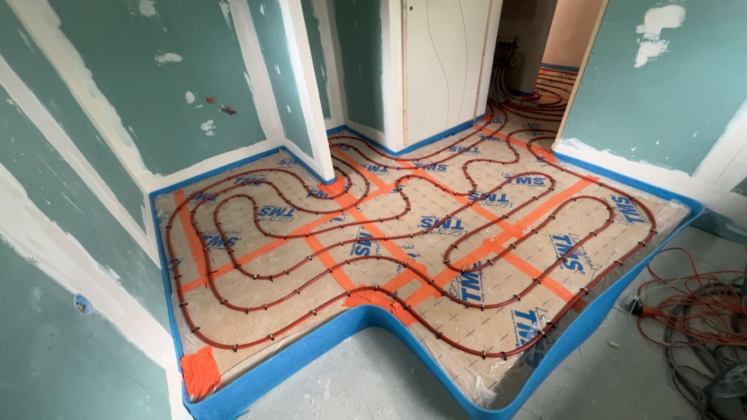 Installation d'un système de chauffage au sol avec tuyaux orange sur isolation, bordure bleue, dans une pièce.