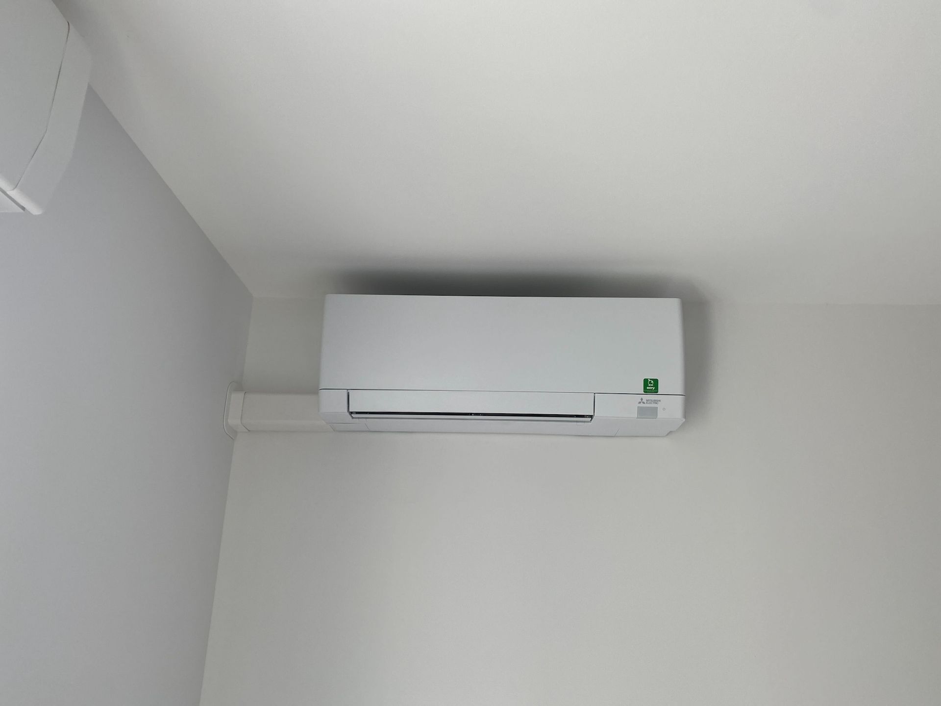 Unité de climatisation blanche fixée sur un mur blanc dans un coin.