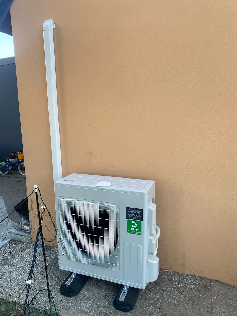 Unité de climatisation avec conduits blancs sur un mur orange.