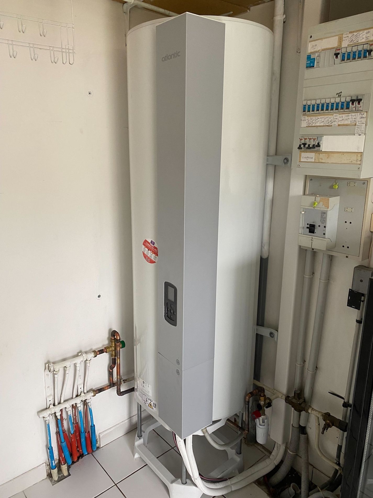 Gros chauffe-eau dans une pièce avec un mur blanc et un tableau électrique.