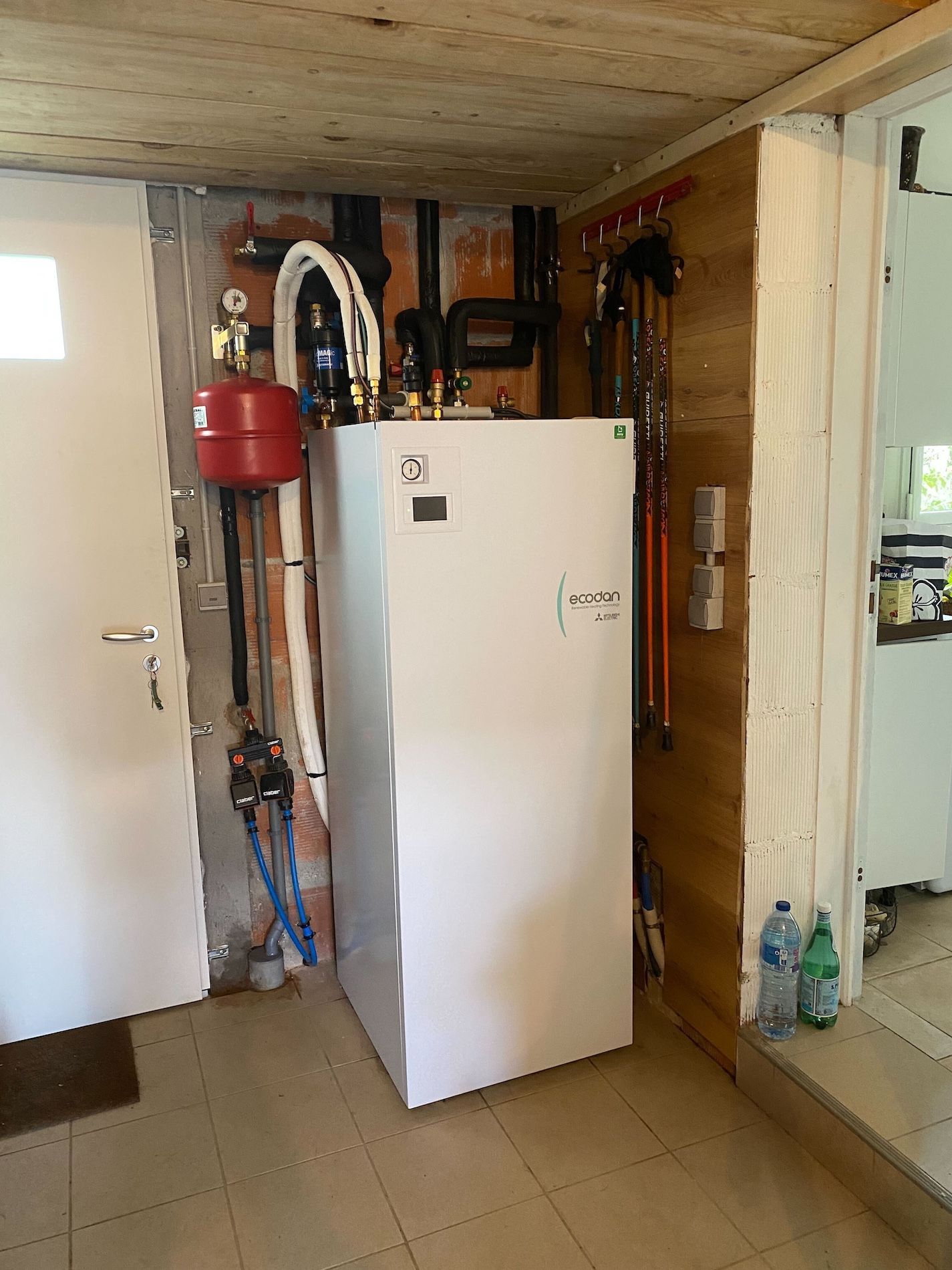 Système de pompe à chaleur blanche dans un local technique, avec tuyauterie et réservoir sous pression rouge.