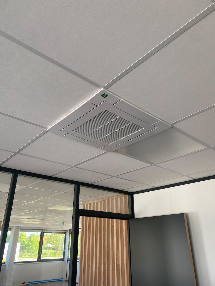 Unité de climatisation fixée au plafond et centrée dans un plafond carrelé blanc. Intérieur de bureau avec murs vitrés.