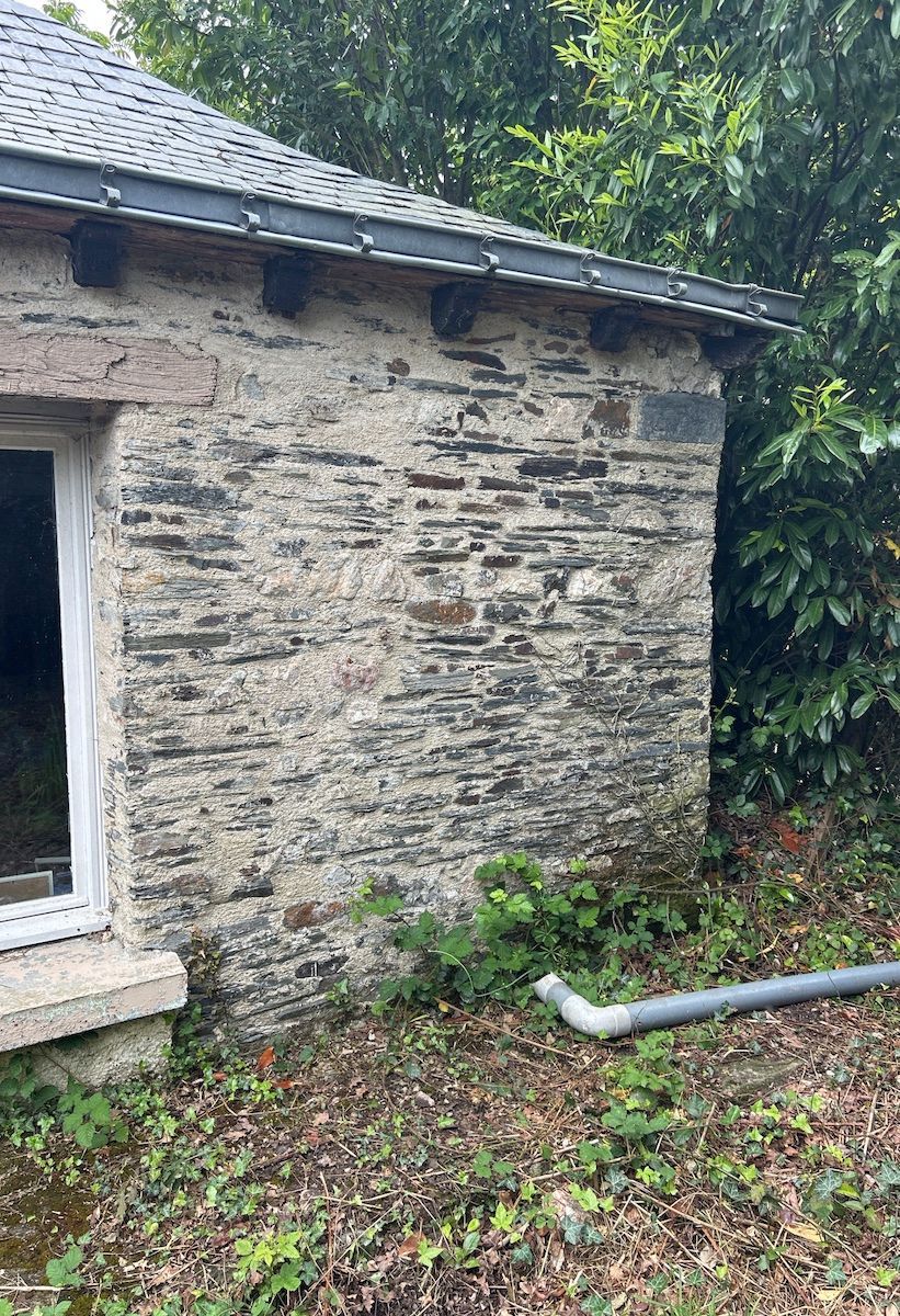 Bâtiment en pierre avec toit en ardoise, murs en pierre grise et noire et encadrement de fenêtre blanc.