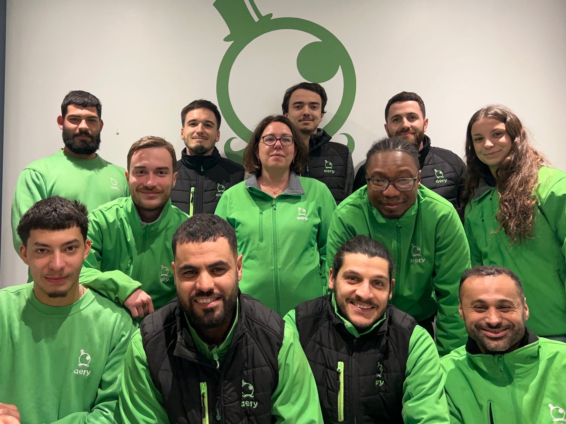 Groupe de personnes vêtues de vert posant devant un logo.