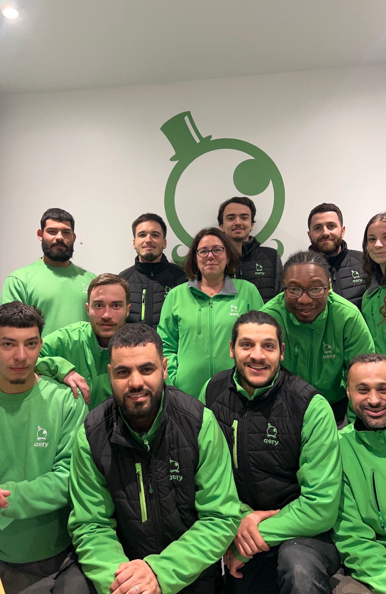 Un groupe de personnes en chemises vertes et gilets noirs pose devant un logo.
