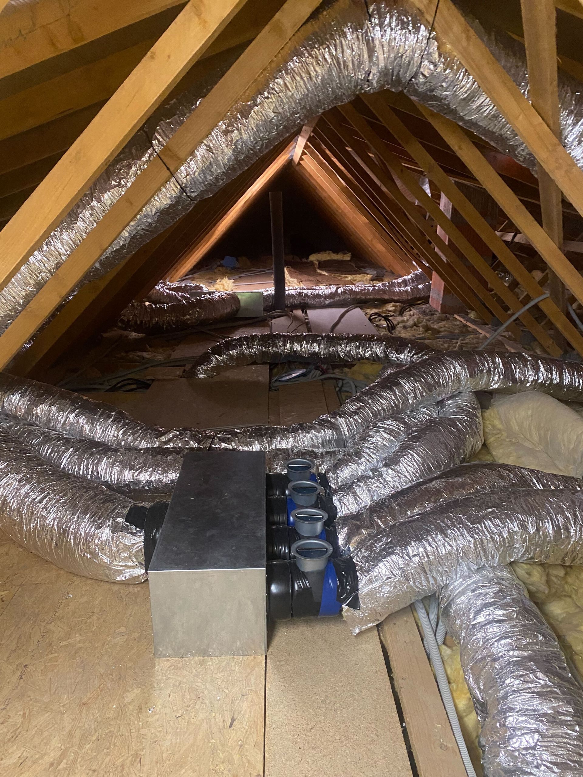 Grenier avec poutres en bois, conduits d'aération en argent et unité de climatisation métallique sur une plateforme en bois.