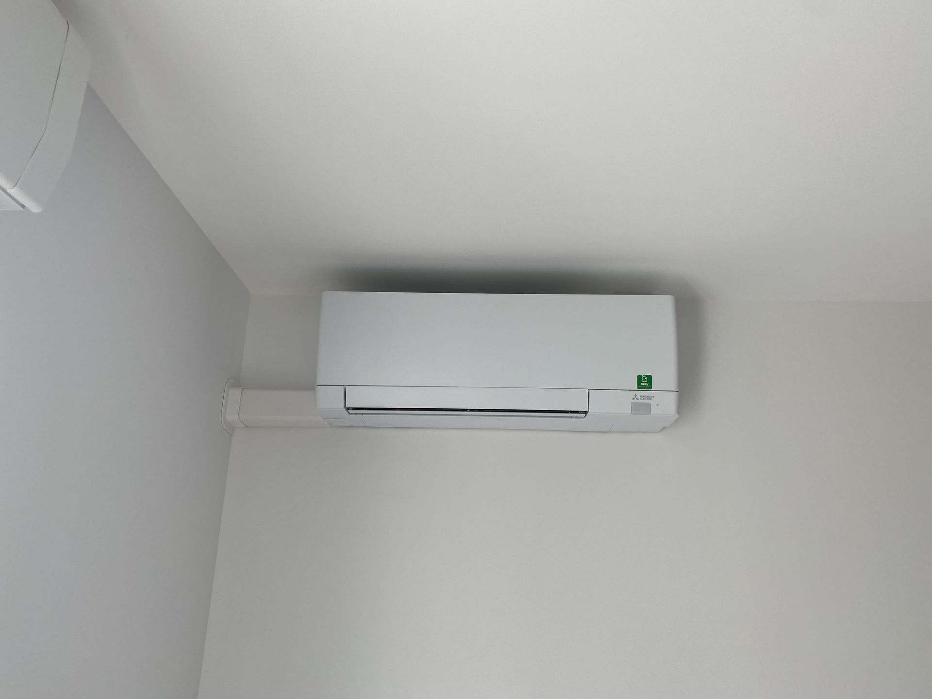 Unité de climatisation blanche fixée sur un mur blanc dans un coin.