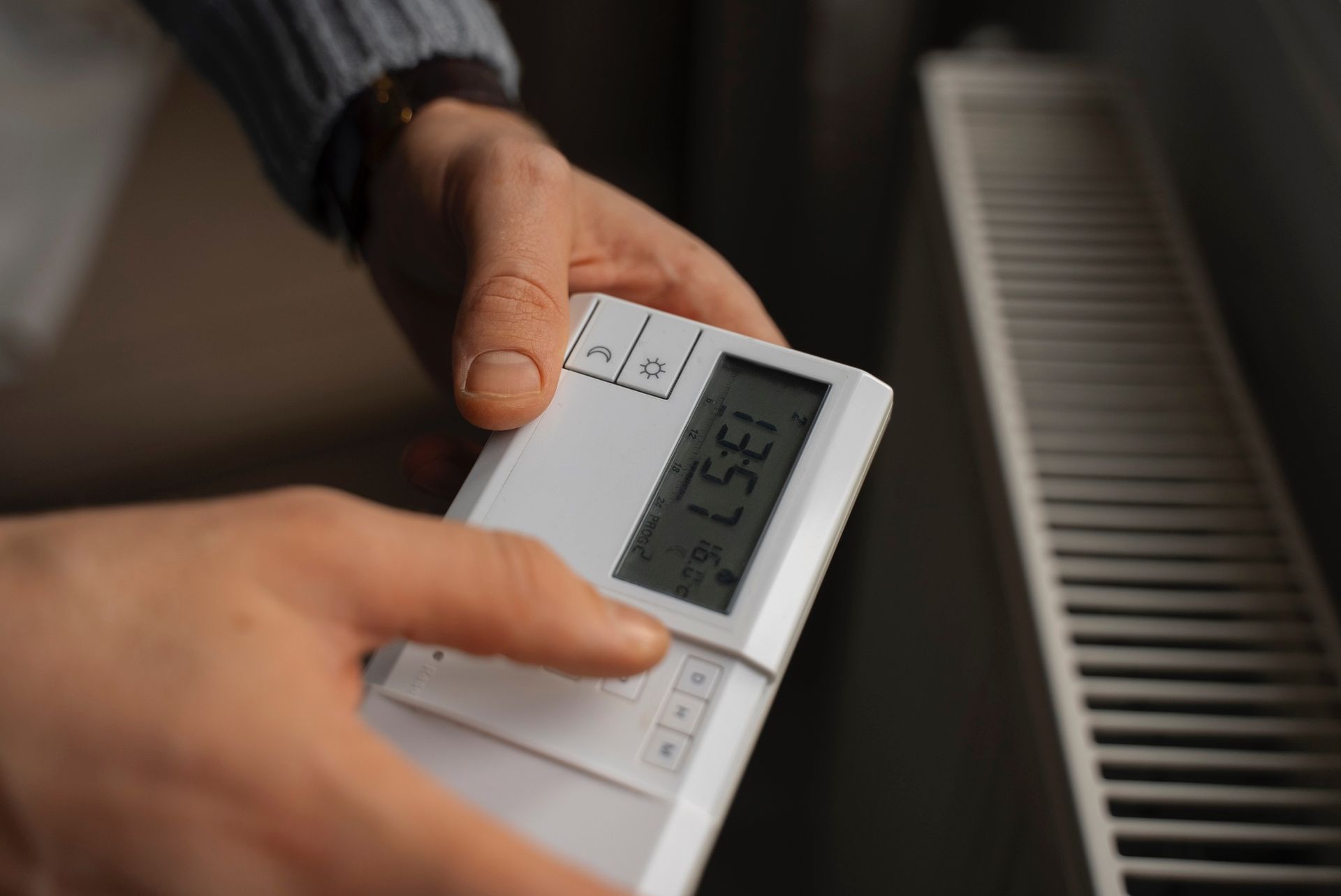 Une personne règle un thermostat blanc près d'un radiateur. L'affichage indique 85,7.