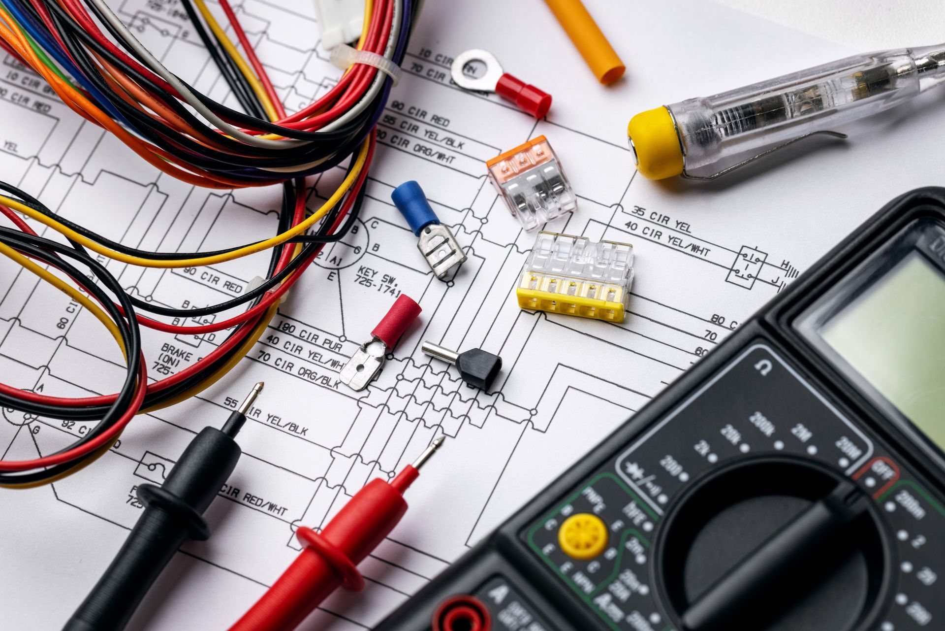 Outils électriques et multimètre sur un schéma de câblage avec fils de couleur et cordons de test.