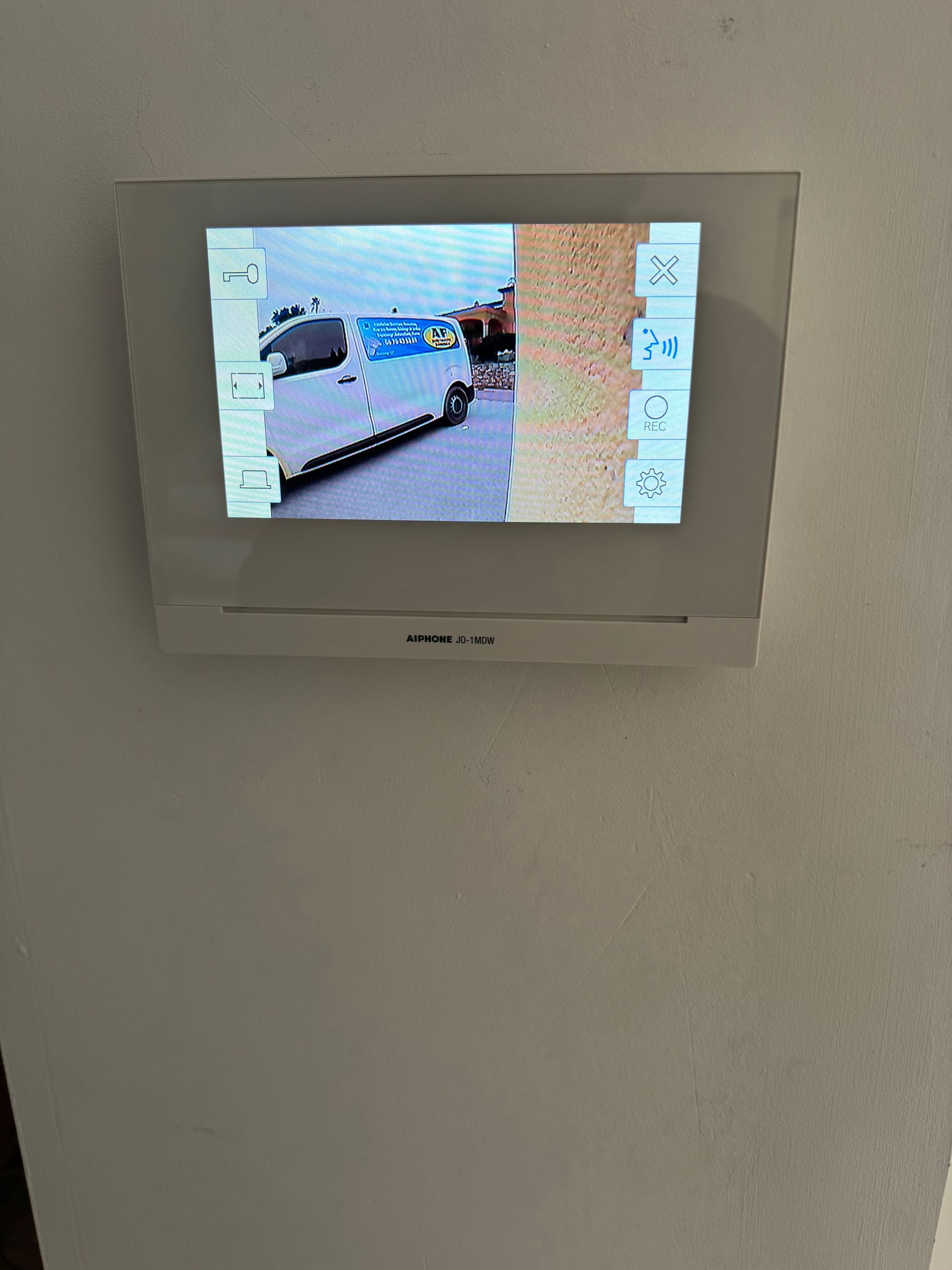 Moniteur vidéo mural montrant un paysage extérieur avec un véhicule blanc stationné.