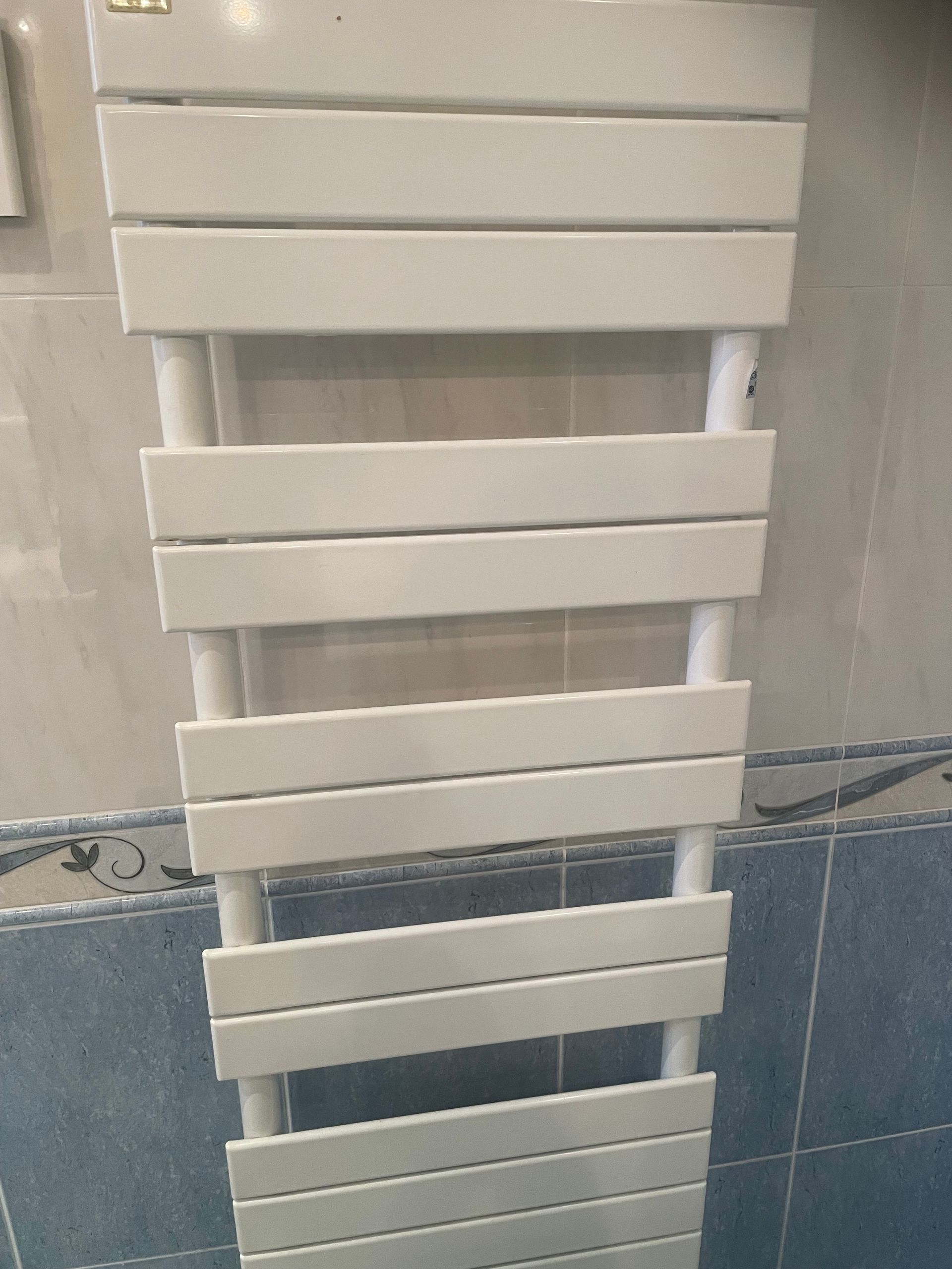 Radiateur sèche-serviettes blanc de style échelle, fixé au mur carrelé de la salle de bain