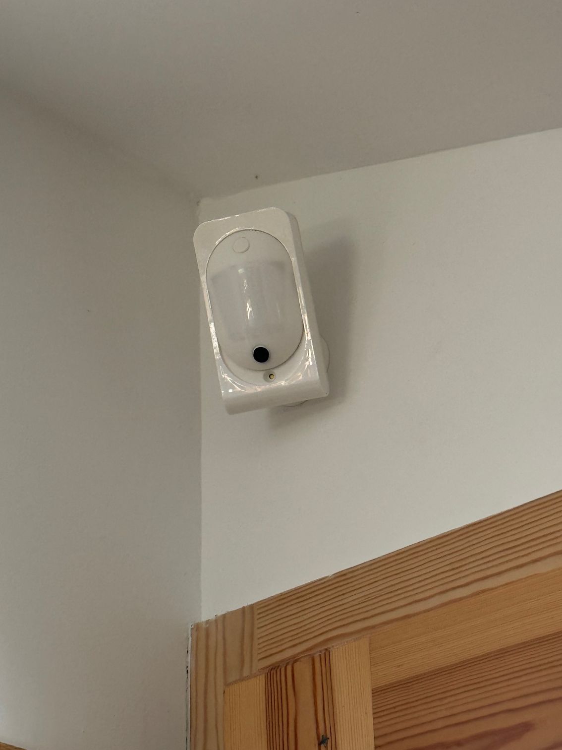 Détecteur de mouvement blanc fixé au mur au-dessus d'un cadre de porte en bois dans un coin de pièce