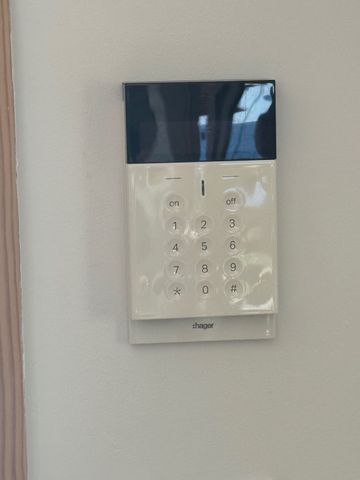 Clavier mural blanc avec panneau supérieur bleu foncé, dans un couloir ou une entrée.