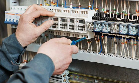 Technicien ajustant le câblage à l'intérieur d'un tableau électrique à l'aide d'outils