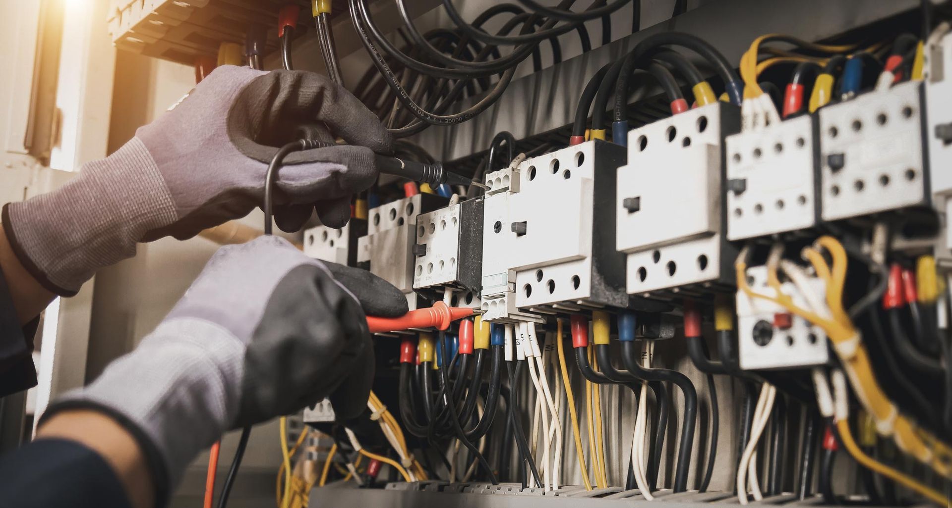Des mains gantées câblent un tableau de commande électrique avec des disjoncteurs et des câbles