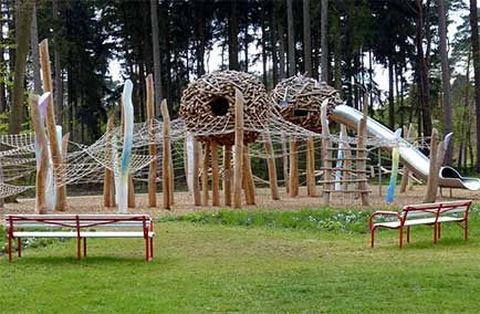 Aire de jeux extérieure avec des structures d'escalade tressées en forme d'arbres et des bancs rouges sur la pelouse